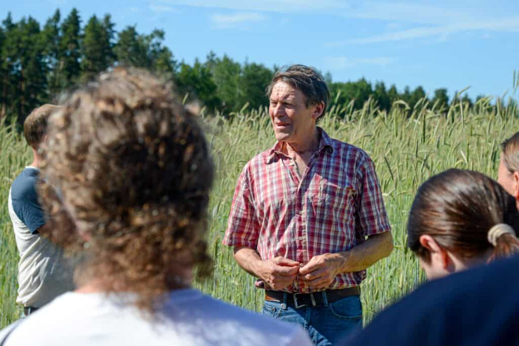 Thomas Björklund Warbro Kvarn står ute på ett spannmålsfält och talar inför besökare på Kvarndagen 2025